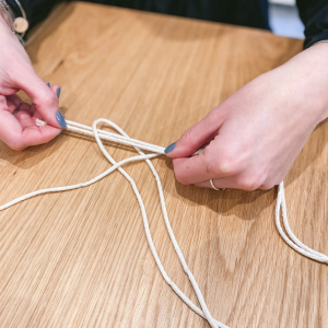 Nimm die 8 Knüpfschnüre doppelt und knüpfe sie so an die 0,5 m Trägerschnur, sodass je Knüpfschnur 2 Fäden nach unten hängen (in der Fachsprache heißt der Knoten „larks head knot“). 