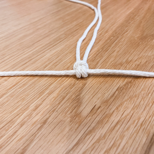 Nimm die 8 Knüpfschnüre doppelt und knüpfe sie so an die 0,5 m Trägerschnur, sodass je Knüpfschnur 2 Fäden nach unten hängen (in der Fachsprache heißt der Knoten „larks head knot“). 