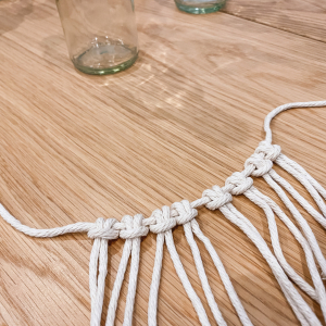 Nimm die 8 Knüpfschnüre doppelt und knüpfe sie so an die 0,5 m Trägerschnur, sodass je Knüpfschnur 2 Fäden nach unten hängen (in der Fachsprache heißt der Knoten „larks head knot“). 