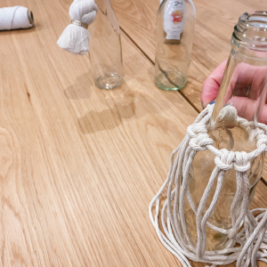 Anschließend fixierst du die Trägerschnur unterhalb des Flaschenhalses an die Flasche, die Knüpffäden sollen nach unten hängen.